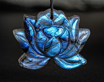 May include: A blue labradorite gemstone carved into a lotus flower pendant. The pendant is hanging from a black cord.