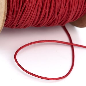 May include: A spool of red elastic cord, wound around a cardboard spool with a rose design. The cord is thin and flexible, and is ideal for crafting and jewelry making.