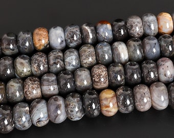 May include: Close-up of a strand of gemstone beads. The beads are barrel-shaped and feature a mix of colors, including gray, brown, and cream. The beads have a polished, glossy finish and are strung together, creating a textured surface.