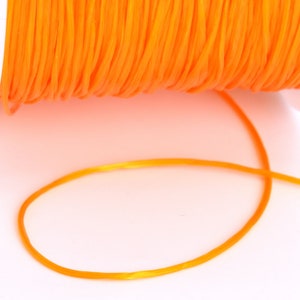 May include: A spool of bright orange string or cord. The string is wound around a white plastic spool and a length of string is hanging off the spool.