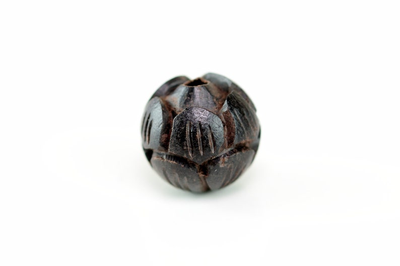 May include: A dark brown wooden bead with a carved, geometric pattern. The bead is round and has a small hole in the center.