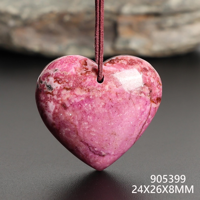May include: A heart-shaped pendant made of pink and white stone, suspended by a maroon cord. The pendant measures approximately 0.94 x 1.02 x 0.31 inches. The surface of the stone has a polished, glossy finish.
