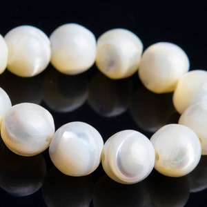 May include: A strand of white pearl-like beads with iridescent shimmer. The beads are round and smooth, and they are strung together on a clear thread.
