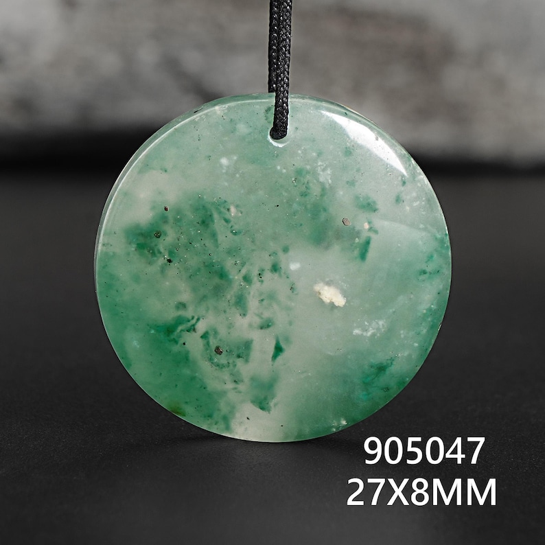 Pu&ograve; includere: Un ciondolo rotondo verde con aspetto marmorizzato, sospeso a un cordino nero. Il ciondolo misura circa 2,7 cm di diametro e 8 mm di spessore. Il testo "905047 27X8MM" &egrave; visibile in basso.