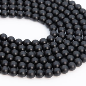 May include: A strand of black matte round beads. The beads are smooth and uniform in size and shape.