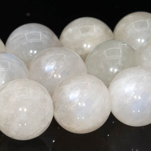 May include: A collection of white moonstone spheres, each with a smooth, polished surface. The spheres are arranged in a row, with the light reflecting off of their surfaces.