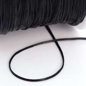 May include: A spool of black elastic cord, with a length of cord unwound and lying on a white surface.