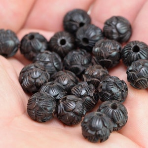 Puede incluir: Una colecci&oacute;n de cuentas de madera negra con intrincados dise&ntilde;os tallados. Las cuentas son redondas y tienen un acabado liso y pulido.