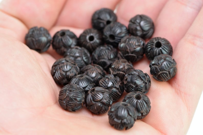Puede incluir: Una colecci&oacute;n de cuentas de madera negra con intrincados dise&ntilde;os tallados. Las cuentas son redondas y tienen un acabado liso y pulido.