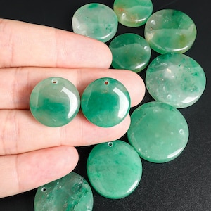 Pu&ograve; includere: Una collezione di pendenti rotondi in pietra preziosa verde lucida, con un foro per l'infilatura. I pendenti, di varie dimensioni e tonalit&agrave; di verde, sono presentati su sfondo nero.