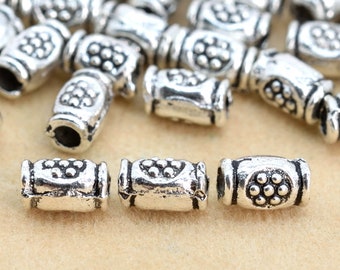 May include: Silver metal beads with a textured design. The beads are cylindrical and have a raised pattern of small circles.