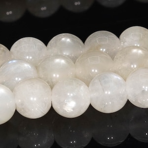 May include: A strand of white moonstone beads, each bead is round and smooth. The beads are arranged in a row, with the light reflecting off of their surfaces.