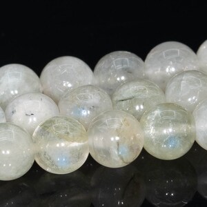 May include: A strand of white gemstone beads with a slight iridescent sheen. The beads are round and smooth, and they are strung on a clear thread.