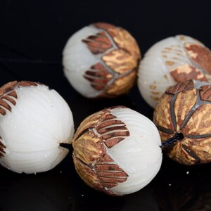 May include: A strand of six white and brown carved beads. The beads are round and have a textured surface. The beads are strung on a black cord.