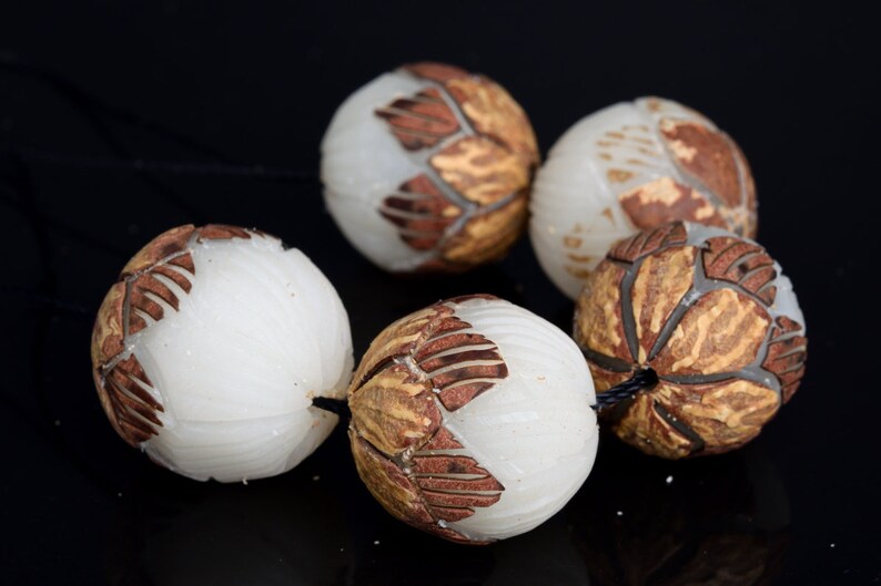 May include: A strand of six white and brown carved beads. The beads are round and have a textured surface. The beads are strung on a black cord.