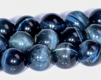 Pode incluir: Um fio de contas de olho de tigre azul. As contas são redondas e têm um acabamento liso e polido. A cor azul é um azul profundo e rico com um leve brilho.