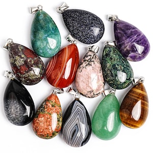 Puede incluir: Surtido de colgantes de piedras preciosas en forma de l&aacute;grima en varios colores y patrones. Los colgantes incluyen piedras verdes, rojas, negras y moradas, cada uno con una fianza plateada para sujetar a una cadena o cord&oacute;n. La colecci&oacute;n muestra variaciones de piedra natural.