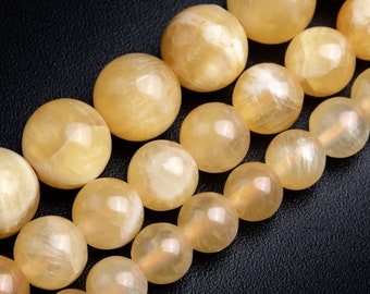 Könnte beinhalten: Eine Kette aus gelben Calcitperlen, jede Perle ist rund und glatt. Die Perlen sind in einer Reihe angeordnet, wobei die Perlen im Vordergrund des Bildes leicht unscharf sind.
