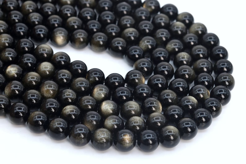 May include: A strand of black obsidian beads with gold flecks. The beads are round and smooth, and they are strung together on a clear thread.