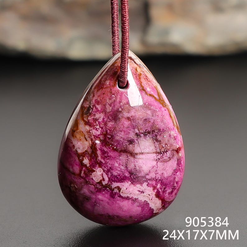 May include: A teardrop-shaped pendant with a vibrant pink and brown marbled pattern, suspended by a maroon cord. The pendant measures 24mm x 17mm x 7mm. The surface is polished and reflective, showcasing the natural stone's unique veining.