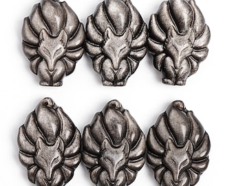 May include: Six metallic silver fox-shaped gemstone carvings. Each carving features a detailed fox face and nine stylized tails. The gemstones have a textured, iridescent finish, and are arranged on a white background.