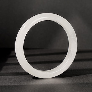 May include: A smooth, circular bangle bracelet crafted from a translucent, milky white stone. The bangle features a polished, rounded exterior surface and a consistent thickness throughout its entire circumference, showcasing a clear, solid structure.