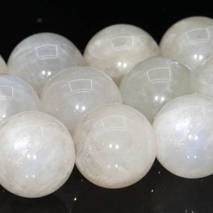 May include: A collection of white moonstone spheres, each with a smooth, polished surface. The spheres are arranged in a row, with the light reflecting off their surfaces.