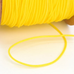 May include: A spool of bright yellow cord, tightly wound and ready for use. The cord is a vibrant, sunny color, and a length of it extends from the spool, suggesting it's ready for crafting or other projects. The spool is made of cardboard.