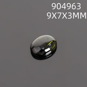 May include: A dark, oval-shaped gemstone with a polished surface. The gem is a deep, translucent green with reflective highlights. The text "904963" and "9X7X3MM" is displayed above the gem. The gem measures approximately 9mm x 7mm x 3mm.