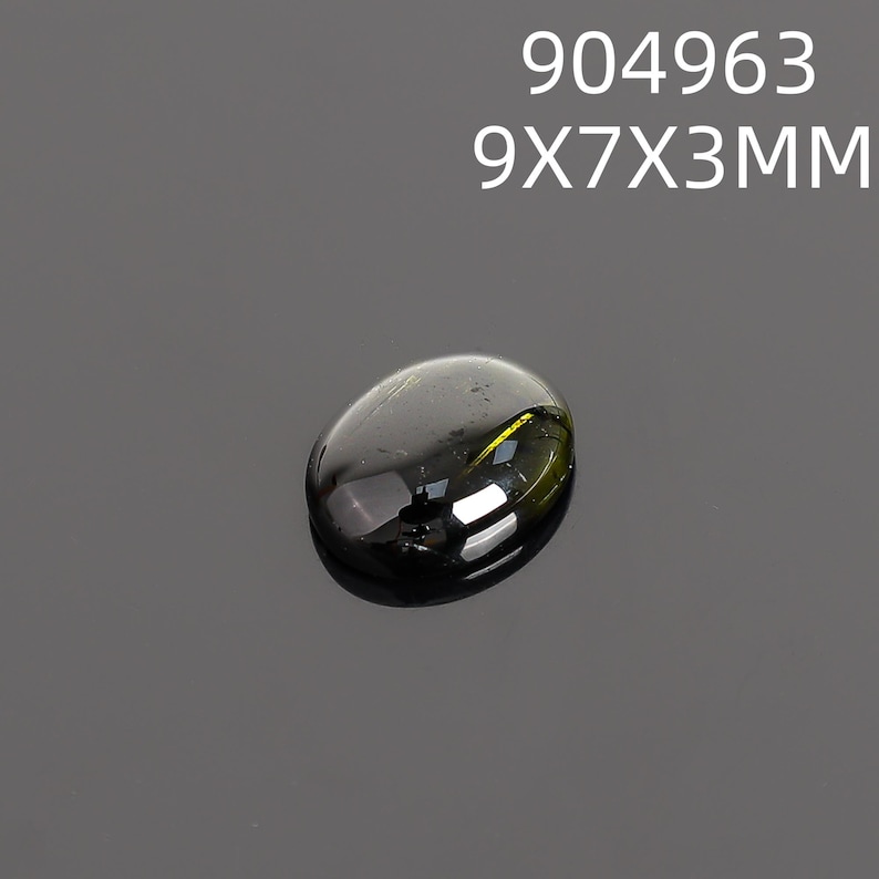 May include: A dark, oval-shaped gemstone with a polished surface. The gem is a deep, translucent green with reflective highlights. The text "904963" and "9X7X3MM" is displayed above the gem. The gem measures approximately 9mm x 7mm x 3mm.