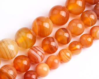 May include: A strand of orange and white agate beads. The beads are round and have a polished finish. The beads are strung on a clear thread.