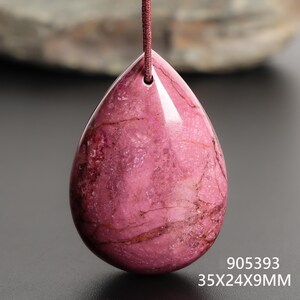 May include: A polished, teardrop-shaped pendant in shades of pink and maroon, suspended by a maroon cord. The gemstone measures approximately 1.4 x 0.9 x 0.4 inches. The pendant has a smooth, glossy surface with natural veining. The text "905393" and "35X24X9MM" are visible.