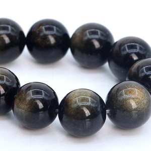 May include: A strand of black gemstone beads with gold flecks. The beads are round and smooth, and they are strung together on a clear thread.