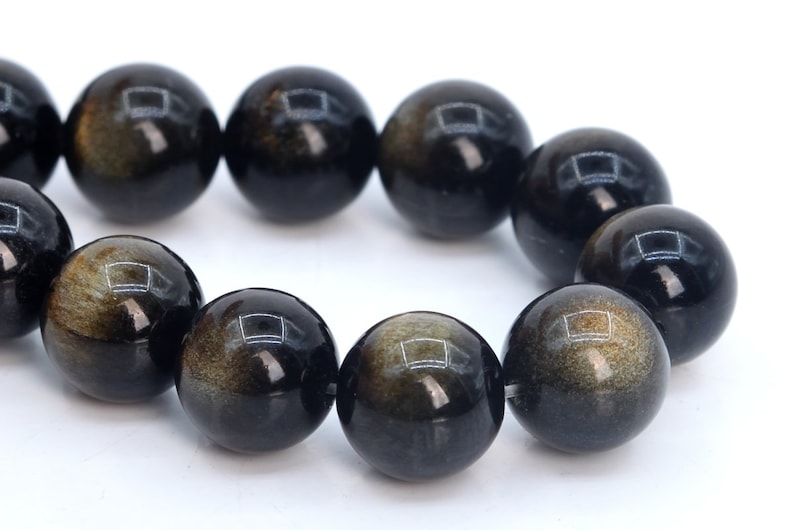 May include: A strand of black gemstone beads with gold flecks. The beads are round and smooth, and they are strung together on a clear thread.
