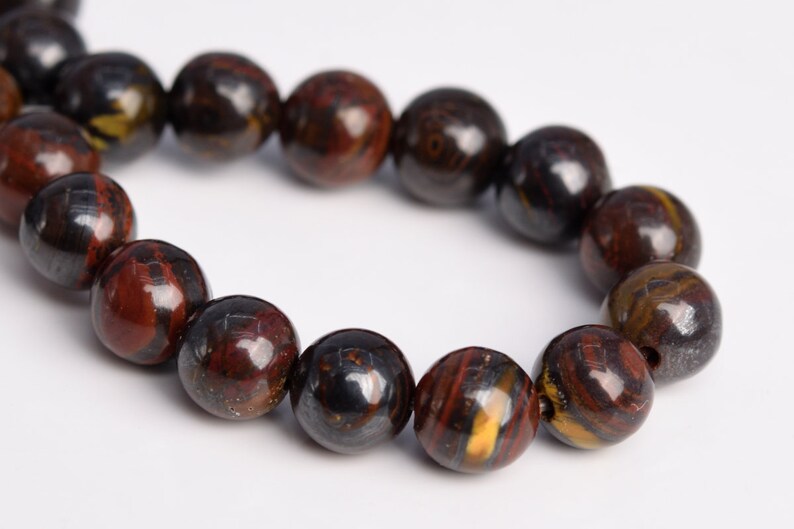 May include: A strand of round, dark brown, red, and gold beads with a metallic sheen. The beads are made of hematite.