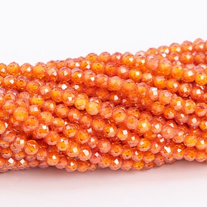 Puede incluir: Una hebra de cuentas de piedras preciosas facetadas de color naranja. Las cuentas son redondas y tienen un acabado brillante y pulido.