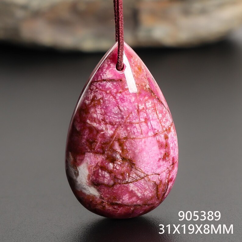 May include: A teardrop-shaped pendant with a pink and brown marbled pattern, suspended by a maroon cord. The pendant's dimensions are 31mm x 19mm x 8mm. The pendant has a glossy finish and a natural, stone-like appearance.