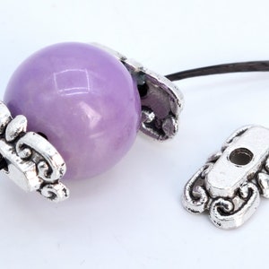 May include: A purple glass bead with silver metal bead caps. The bead caps have a decorative design.