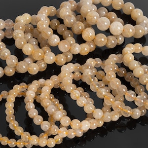 May include: A collection of golden rutilated quartz bracelets. The bracelets are made of round beads and are stacked on top of each other.