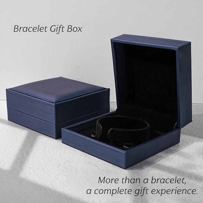May include: Two square navy blue bracelet gift boxes with a textured finish. One box is closed, and the other is open, revealing a black velvet interior with a black circular bracelet holder. Text reads: Bracelet Gift Box. More than a bracelet, a complete gift experience.