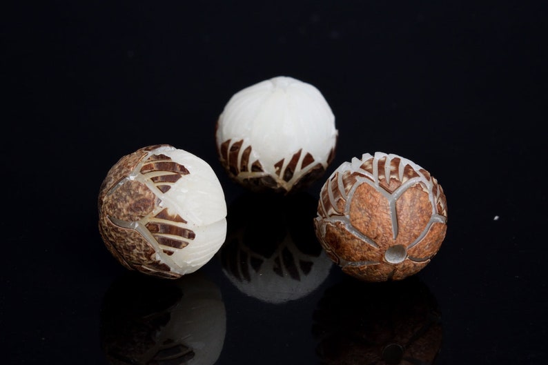 May include: Three round wooden beads with intricate carved designs. The beads are white and brown and have a glossy finish.