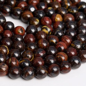 May include: A strand of round, dark brown, red, and gold gemstone beads. The beads have a polished, shiny finish.