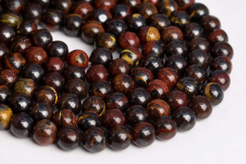 May include: A strand of round, dark brown, red, and gold gemstone beads. The beads have a polished, shiny finish.