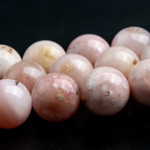 May include: A close-up of a strand of pink opal beads. The beads are round and smooth, with a variety of shades of pink and white.
