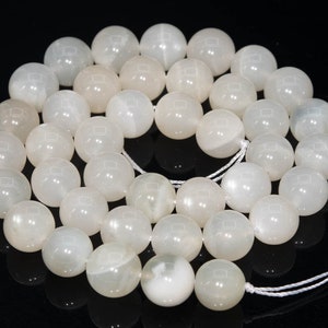 May include: A strand of white moonstone beads, each bead is round and smooth. The beads are strung on a white cord and are ready to be used for jewelry making.