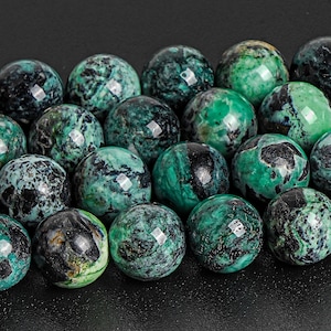May include: A collection of round, green and black gemstone beads. The beads have a mottled, marbled appearance.