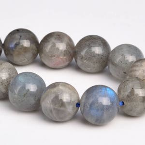 May include: A strand of round, gray labradorite beads with iridescent blue flashes. The beads are strung on a blue cord.