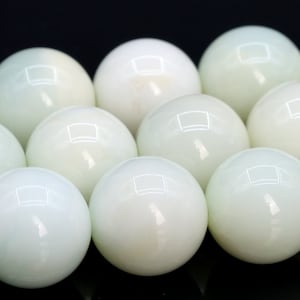 May include: A collection of smooth, white, round beads with a slight green tint. The beads are arranged in a close-up view, showcasing their glossy surface.