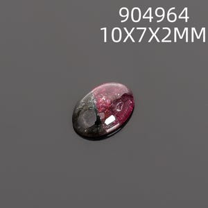May include: An oval-shaped gemstone with a dark red and black color gradient. The gem measures approximately 10mm x 7mm x 2mm. The text "904964" and "10X7X2MM" is displayed above the gem.