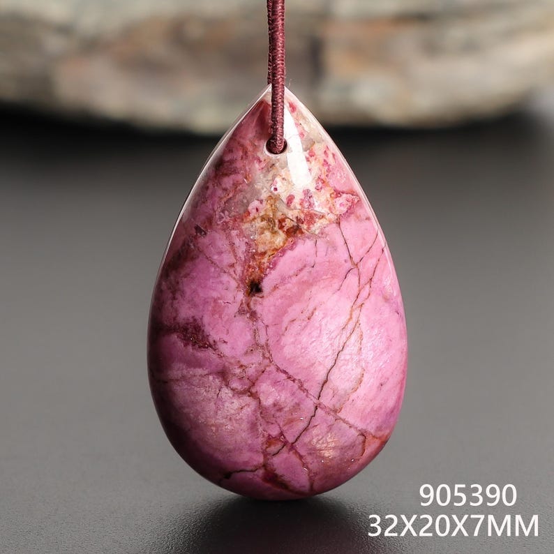 May include: A teardrop-shaped pendant with a pink and white marbled pattern, suspended by a maroon cord. The gemstone measures approximately 1.26 x 0.79 x 0.28 inches. The pendant has a polished surface with visible natural veining. The number "905390" and the dimensions are printed on the bottom.